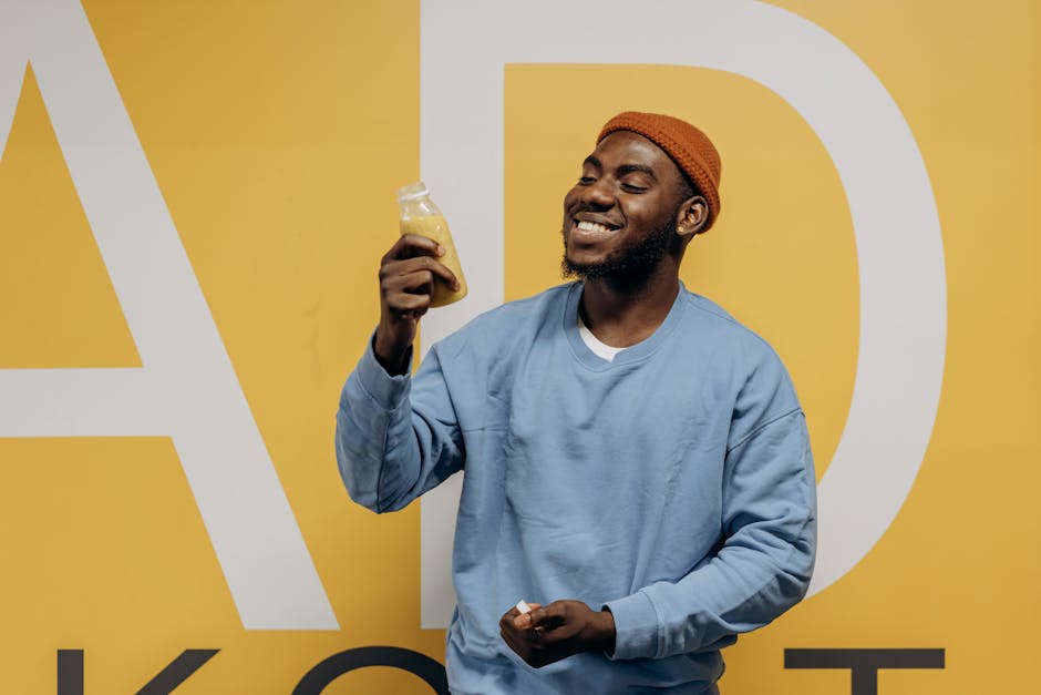 Happy man in casual wear enjoying a healthy juice against a vibrant yellow background.