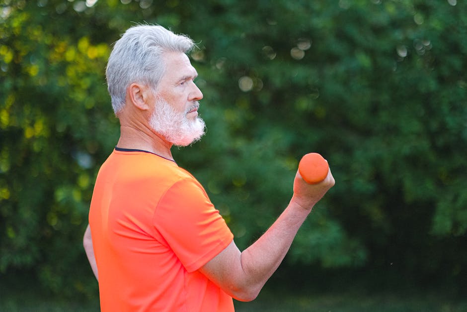 Side view of concentrated senior man in sportswear doing exercise with dumbbells for arms in daytime