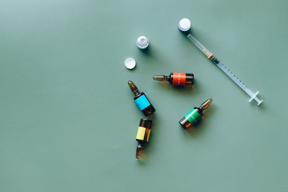 Flat lay of medical ampoules and syringe on a green background, ideal for healthcare themes.