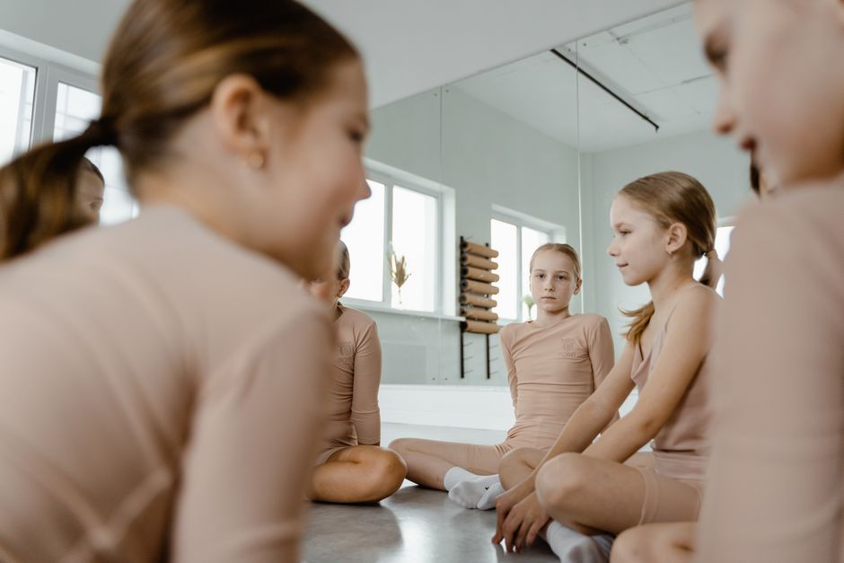 A group of young girls practicing ballet, sitting on the dance studio floor.
