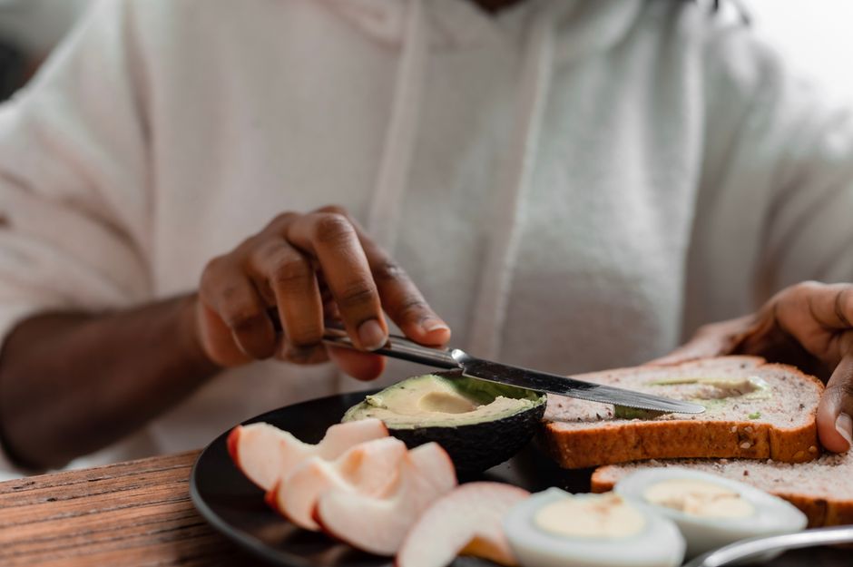 Close-up of hands preparing avocado toast with boiled eggs and apple slices, ideal for health-focused meals.