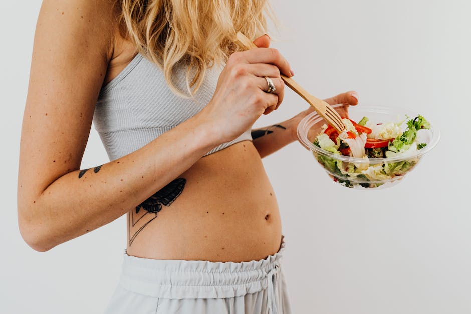 Close-up of a woman in a crop top enjoying a fresh salad indoors.