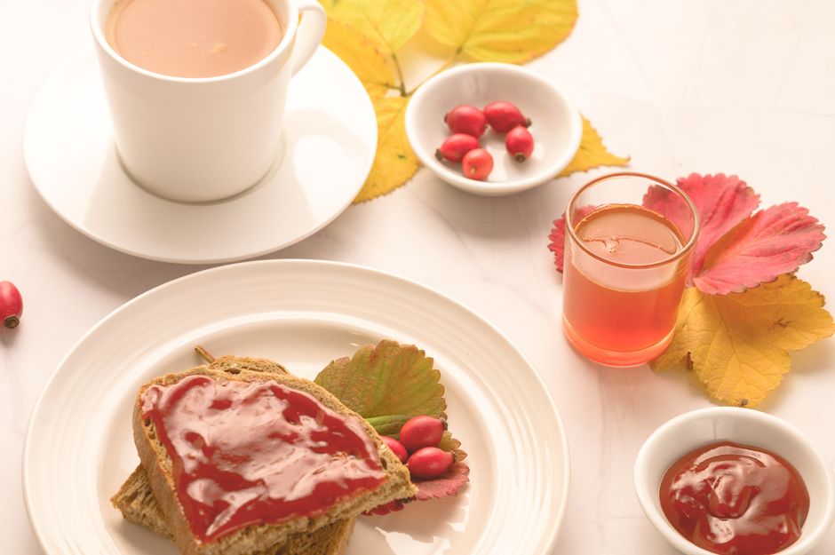 Warm autumn breakfast setup with tea, toast, and rosehip jelly on a fall-themed table setting.