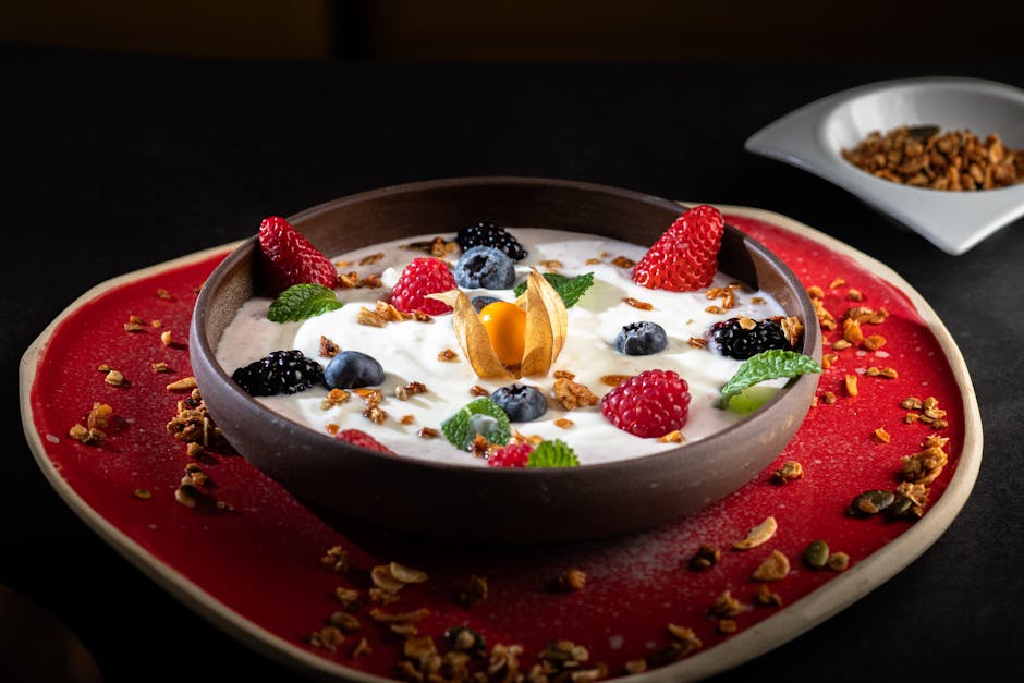 A delicious yogurt bowl topped with fresh berries, granola, and mint leaves, served on a vibrant red plate.