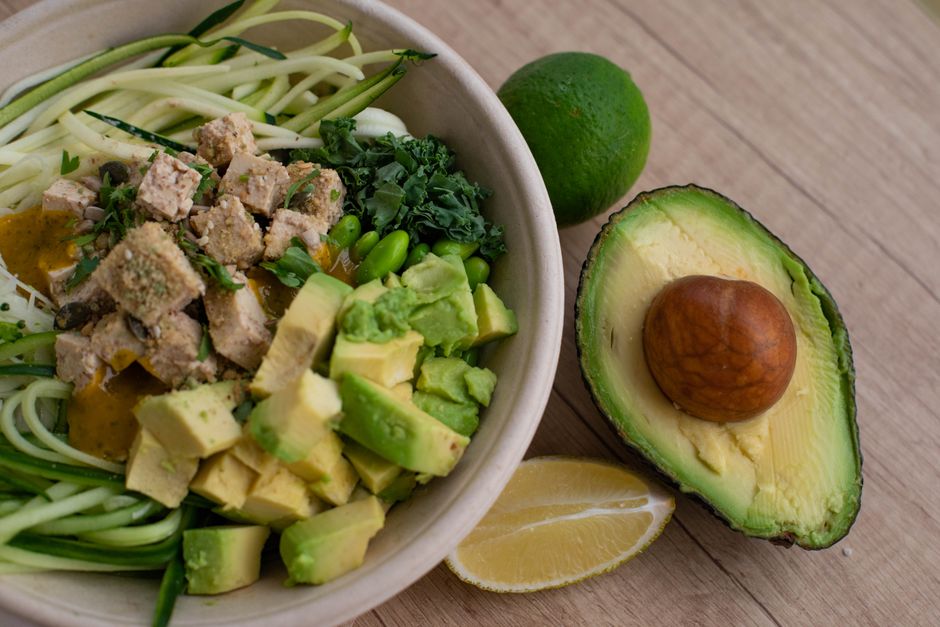 Delicious vegan bowl with zoodles, avocado, tofu, and greens on a wooden table.