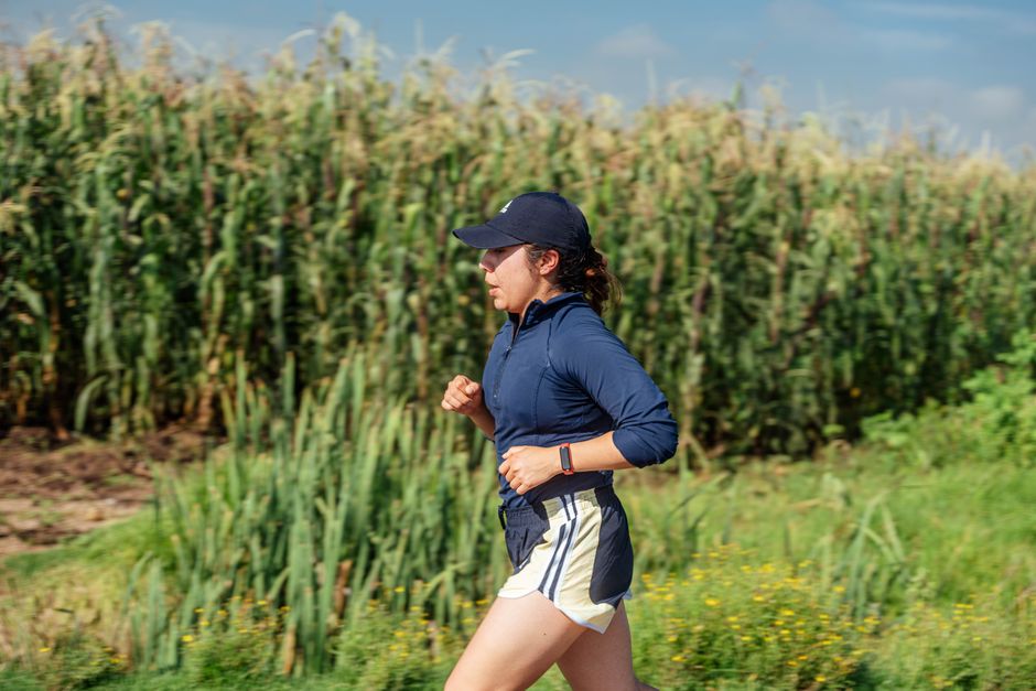 Female jogger running through a rural cornfield on a sunny day.
