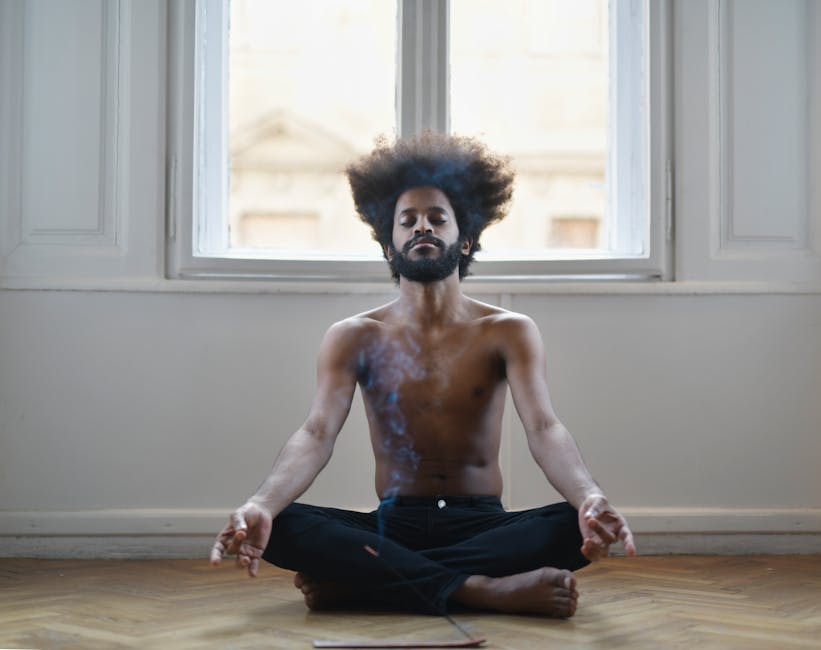 Shirtless man meditating on the floor, surrounded by soothing incense smoke in a tranquil room.