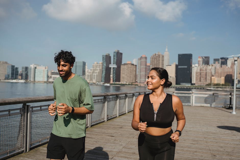 A man and woman jogging on a sunny day with a city skyline in the background.