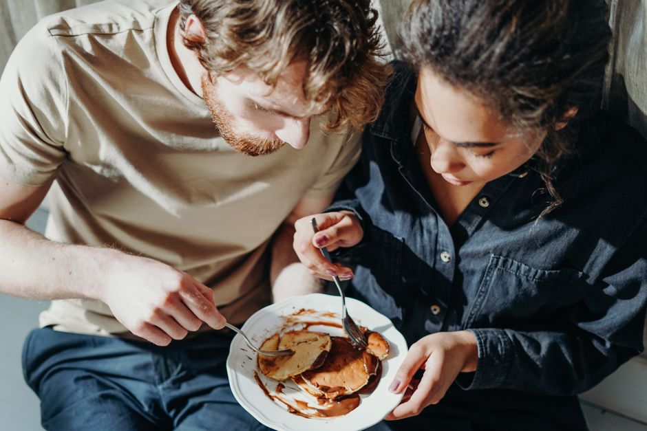 A couple shares a delightful pancake breakfast indoors under morning sunlight.