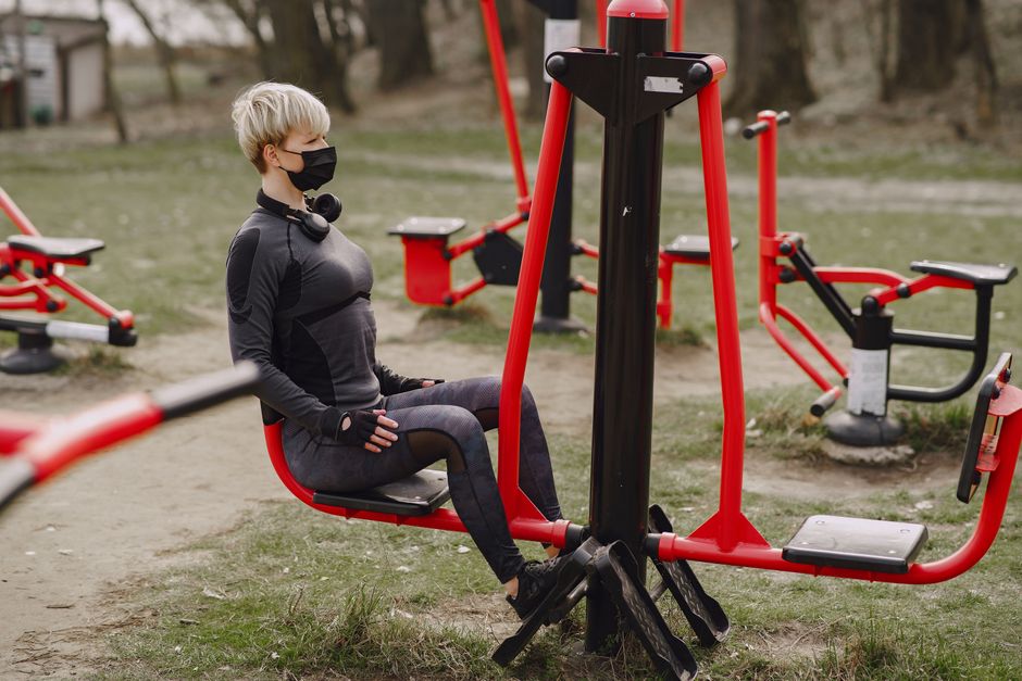 Side view full length of determined sportswoman in activewear and black protective mask doing legs exercise on street workout equipment