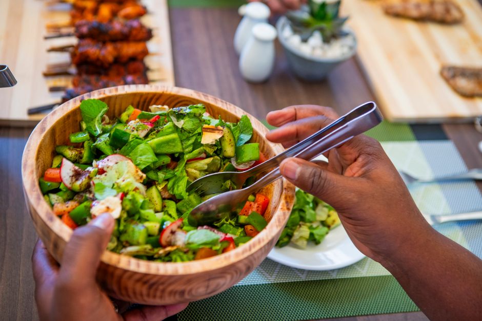 A vibrant, fresh salad in a wooden bowl served with grilled skewers on a table in Nairobi, Kenya.
